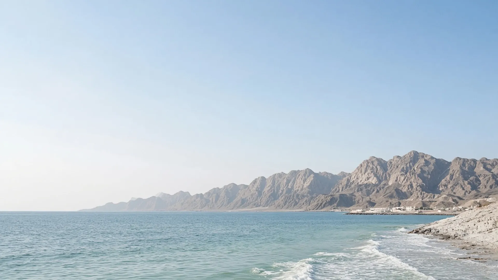 Calm Omani sea meeting rugged mountains near Muscat at first light